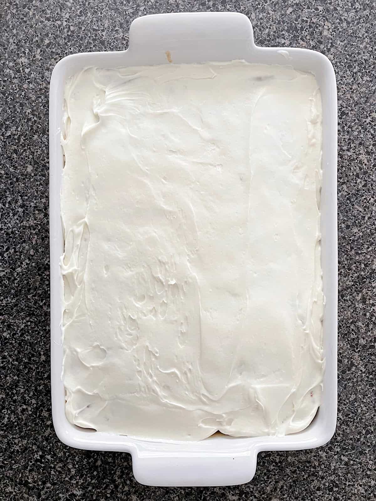 A cinnamon roll poke cake with cream cheese frosting in a white baking dish.