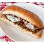A Philly Cheesesteak Sloppy Joe on a white plate with a red and white kitchen towel.