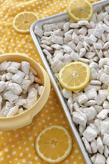 Lemon Pie Muddy Buddies in a yellow bowl and on a baking sheet.
