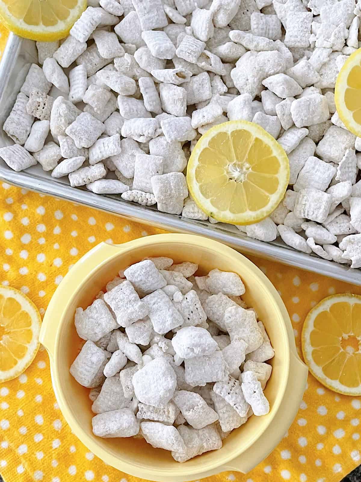 Lemon Pie Muddy Buddies in a yellow bowl and on a baking sheet.
