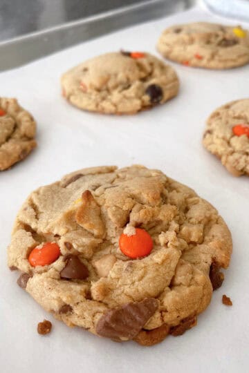 Reese's peanut butter cookies filled with peanut butter chips, peanut butter cups, and Reeses Pieces on a baking sheet.