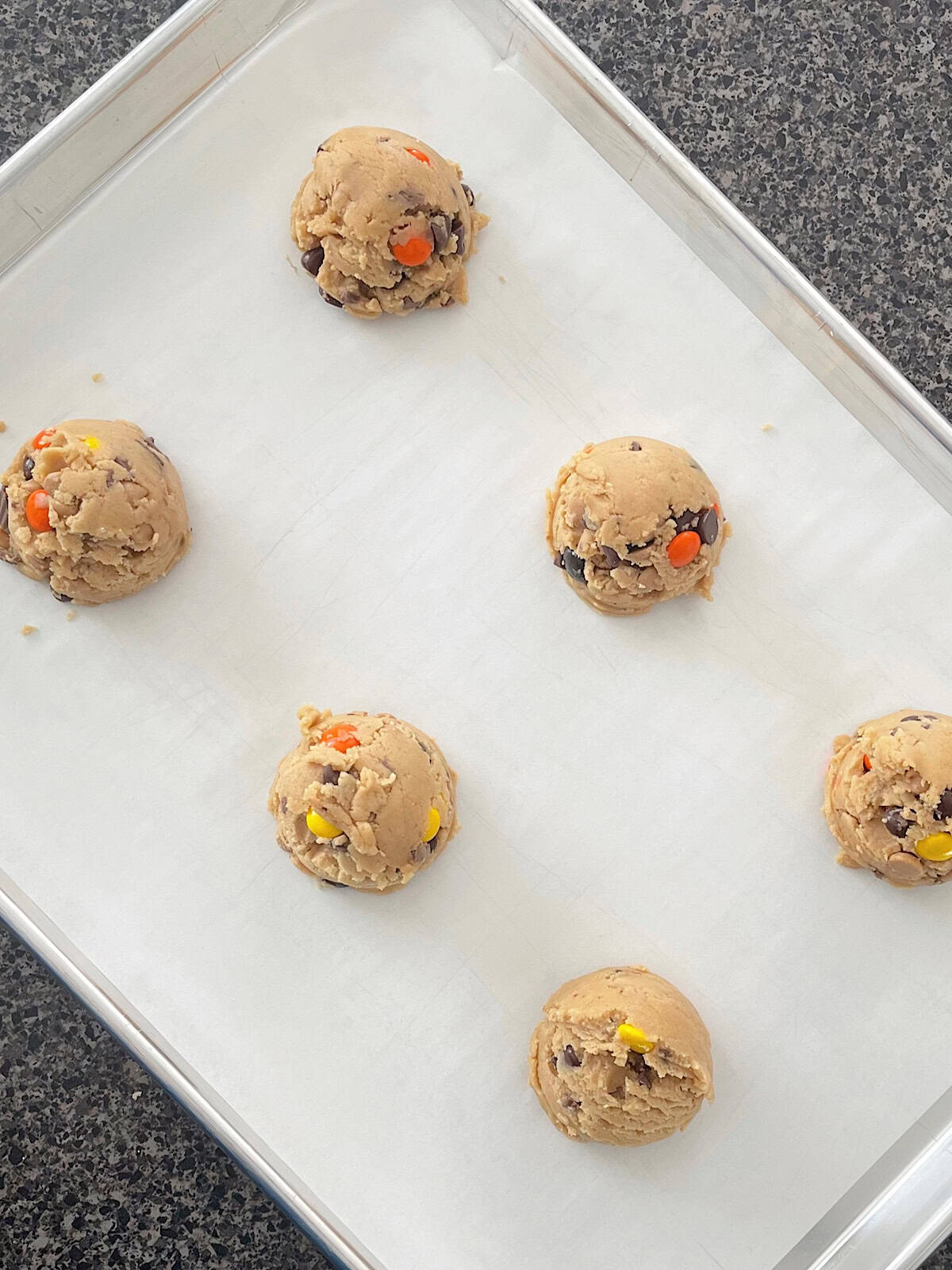 Reese's peanut butter cookies filled with peanut butter chips, peanut butter cups, and Reeses Pieces on a baking sheet.