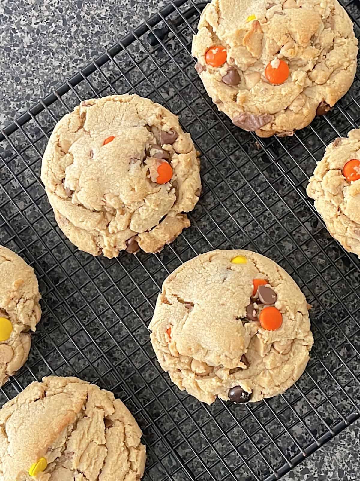 Reese's peanut butter cookies filled with peanut butter chips, peanut butter cups, and Reeses Pieces on a cooling rack.