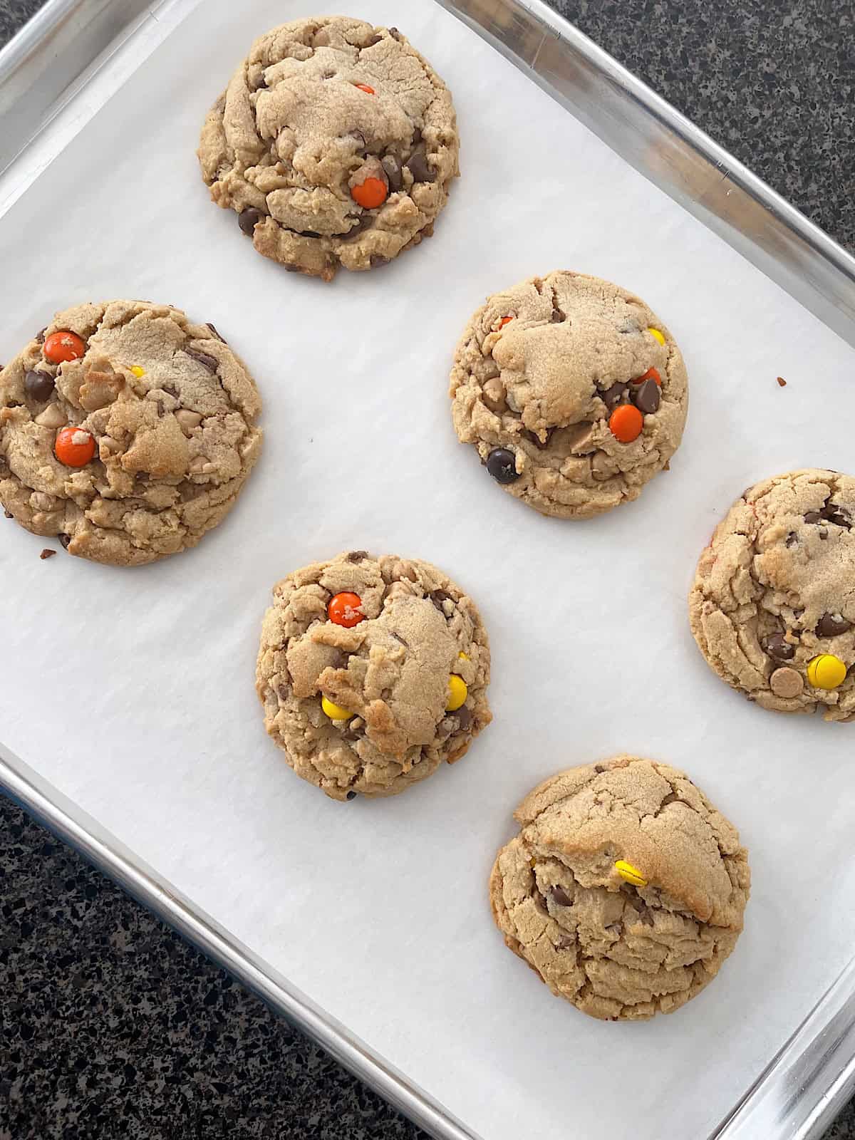 Reese's peanut butter cookies filled with peanut butter chips, peanut butter cups, and Reeses Pieces on a baking sheet.