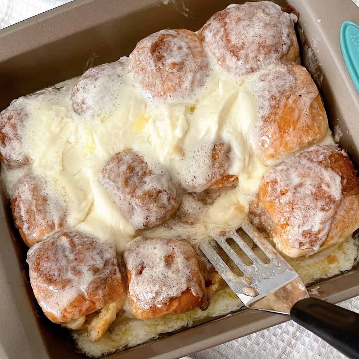 Hawaiian rolls with cinnamon roll filling and icing in a baking pan.