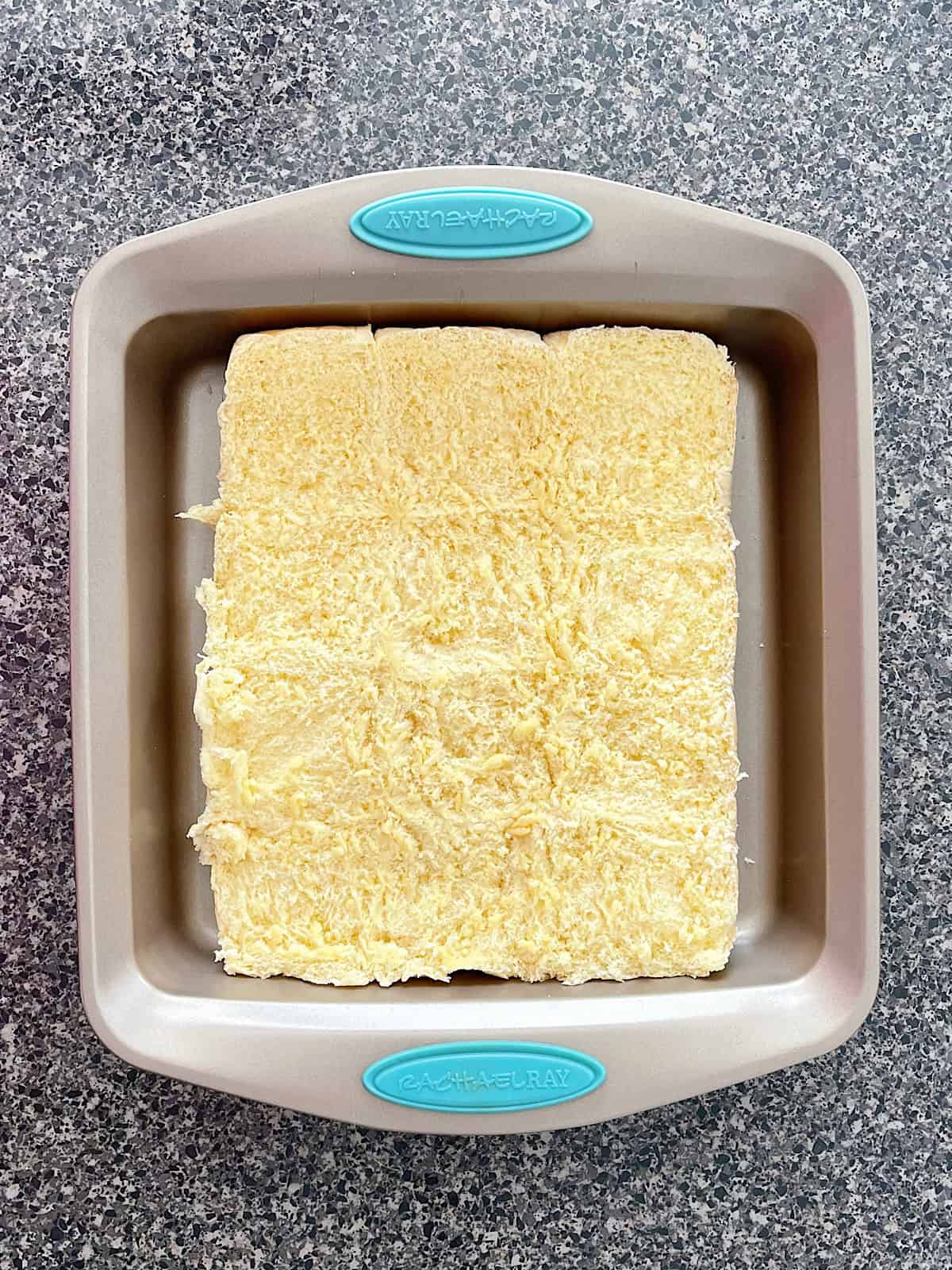 The bottom half of a dozen Hawaiian rolls in a baking pan.