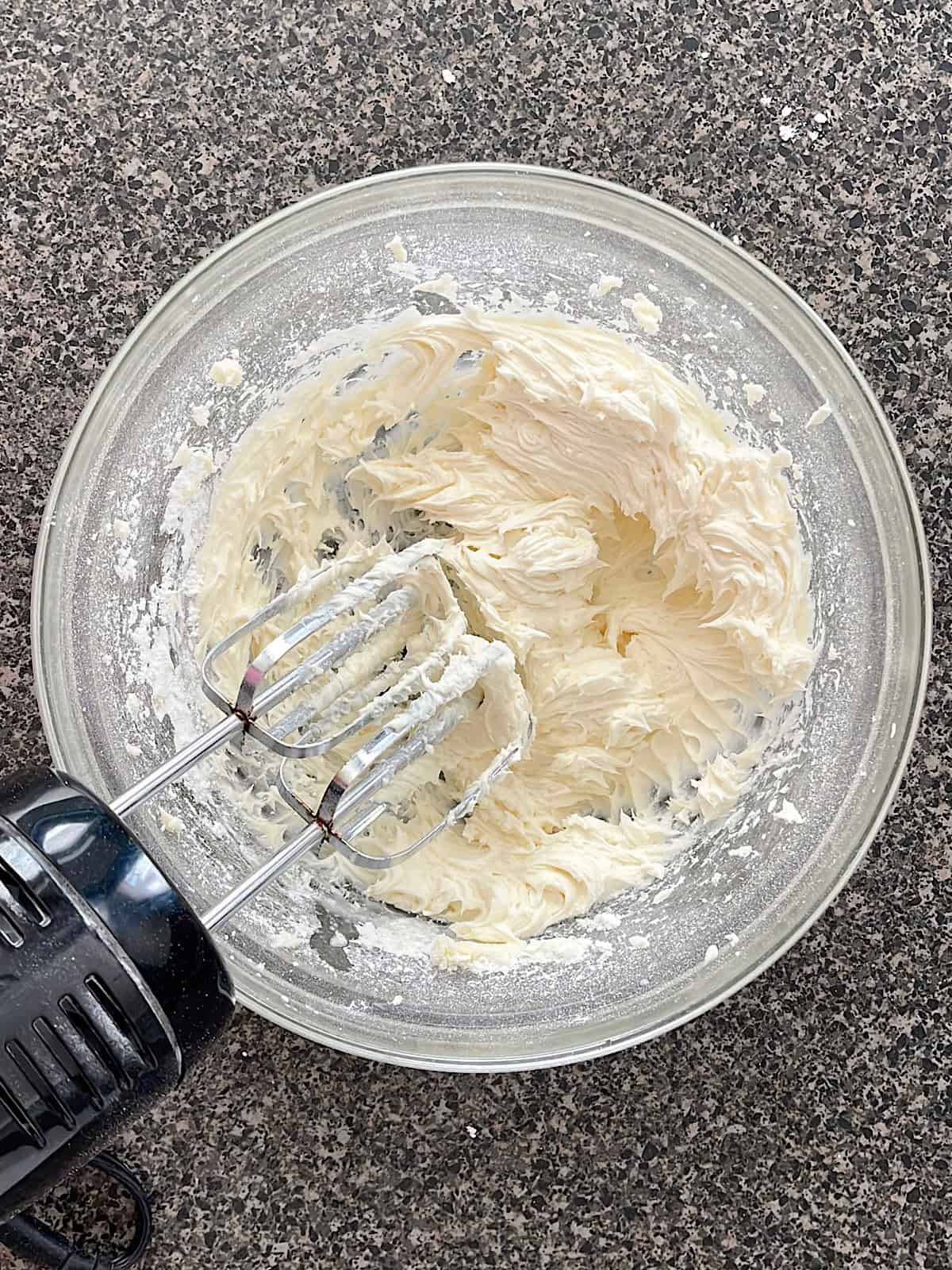 Frosting in a mixing bowl with and hand mixer.