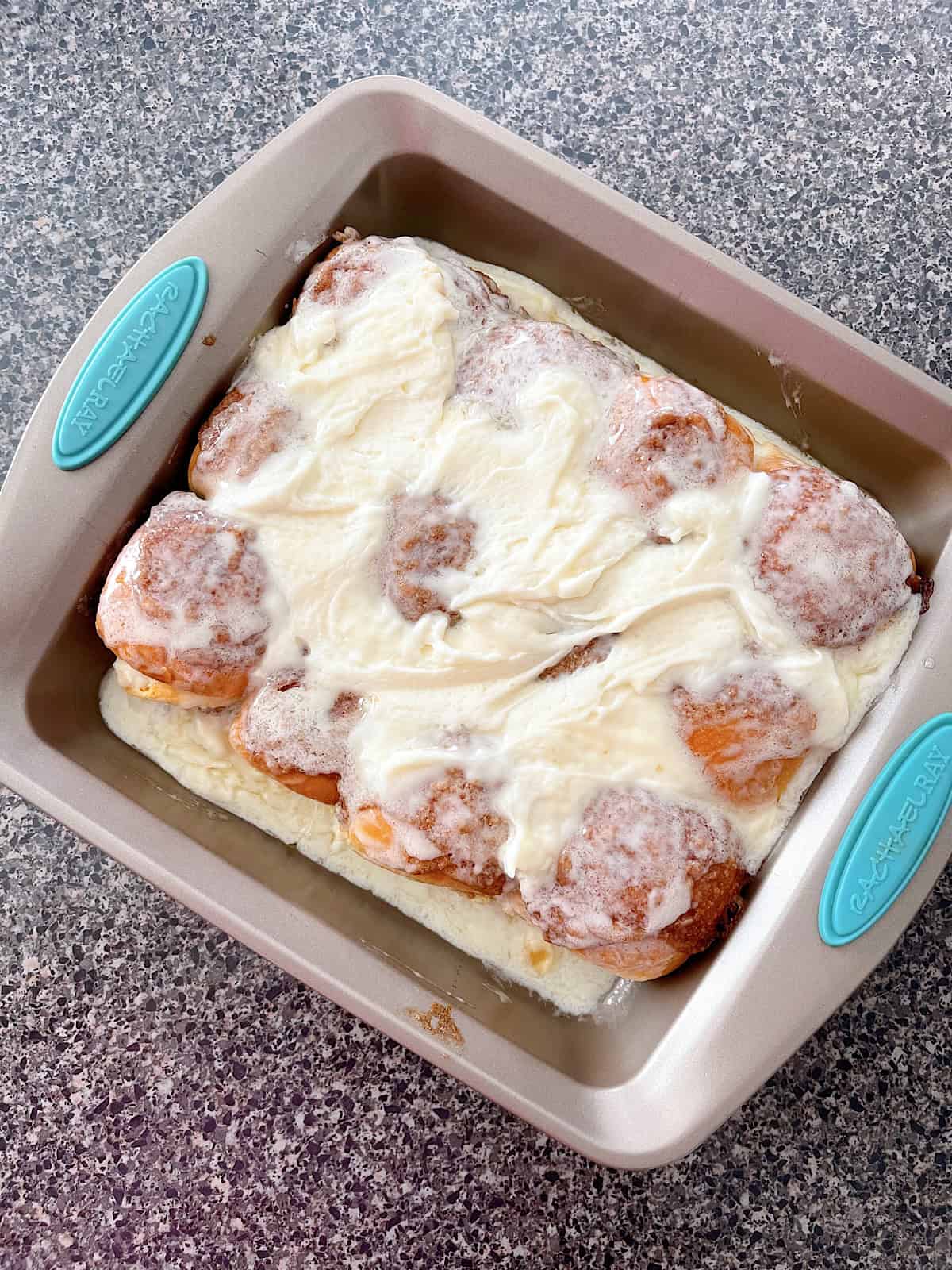 Hawaiian rolls with cinnamon roll filling and icing in a baking pan.
