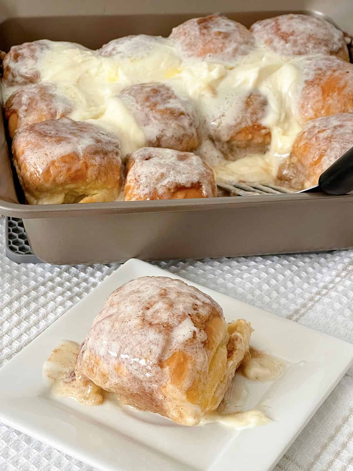 Hawaiian rolls with cinnamon roll filling and icing in a baking pan.