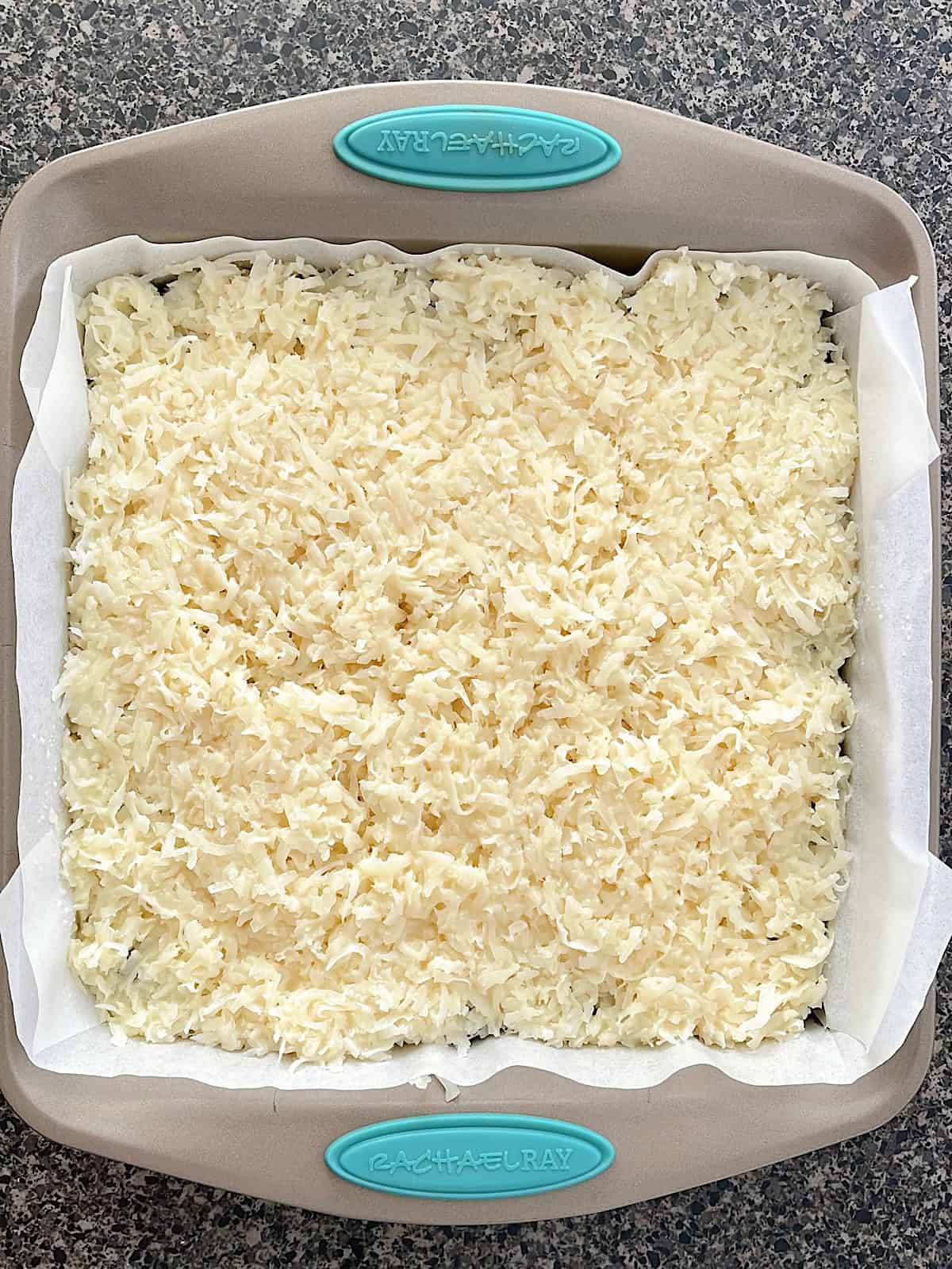 Coconut layer on top of brownies in a baking dish.