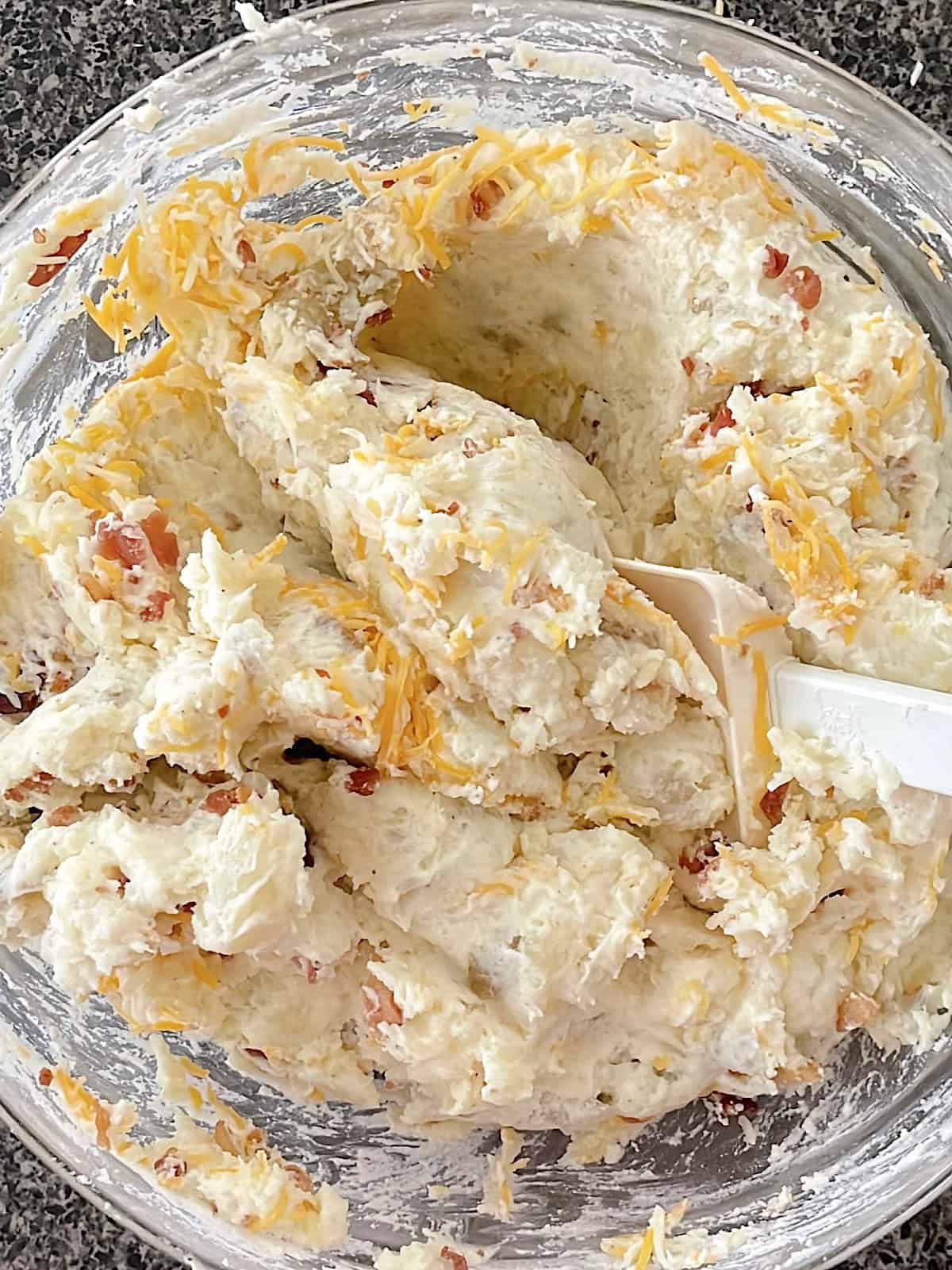 Mashed potatoes with cheese, bacon, sour cream, cream cheese, and spices in a mixing bowl.