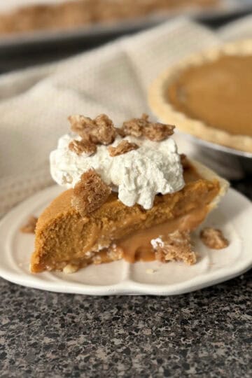 A slice of Milk Bar Pumpkin Caramel Pie topped with whipped cream and streusel.