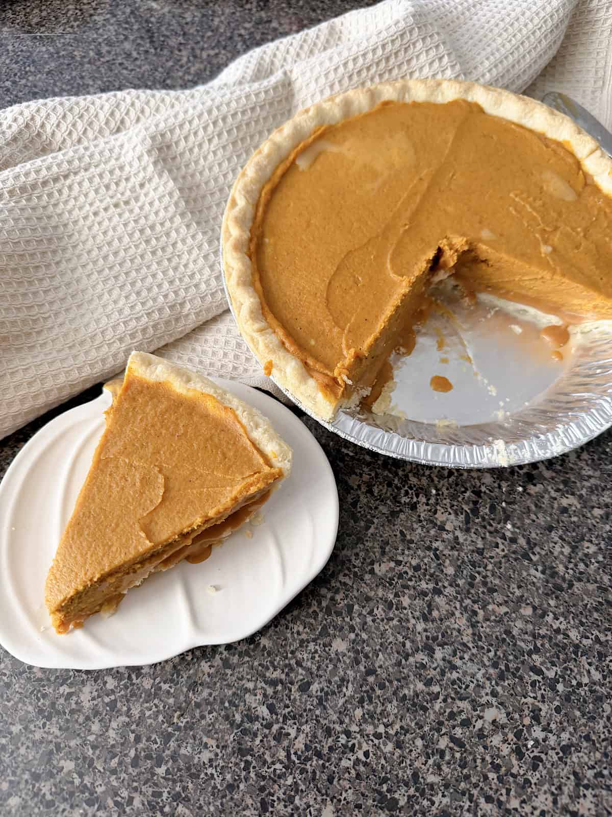 A pumpkin pie with a slice on a white pumpkin-shaped plate.
