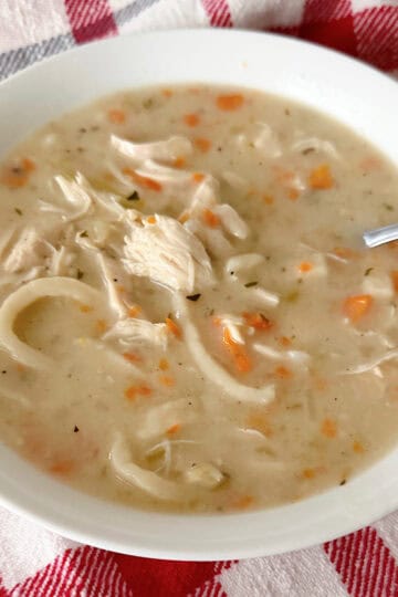 A bowl of creamy chicken noodle soup on a red and white towel.