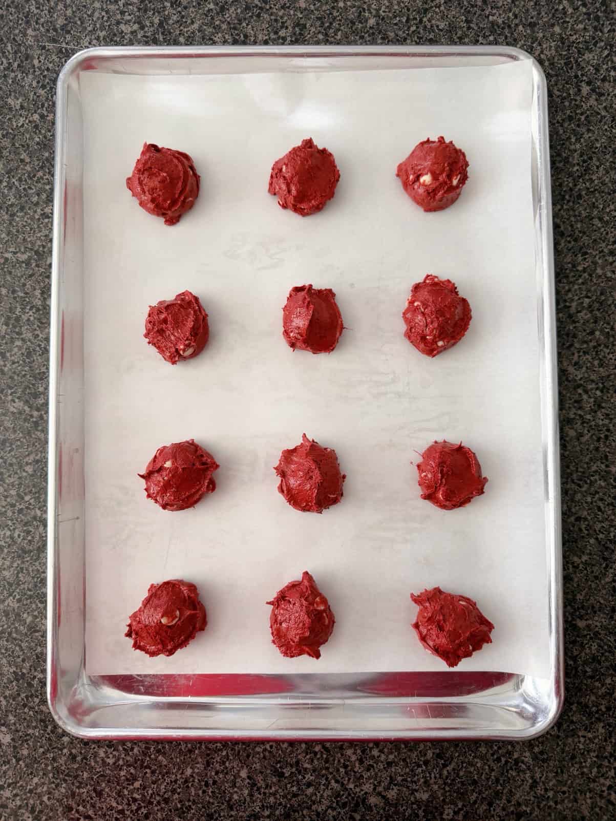 Red Velvet Cookie Dough Balls on a parchment paper-lined baking sheet.