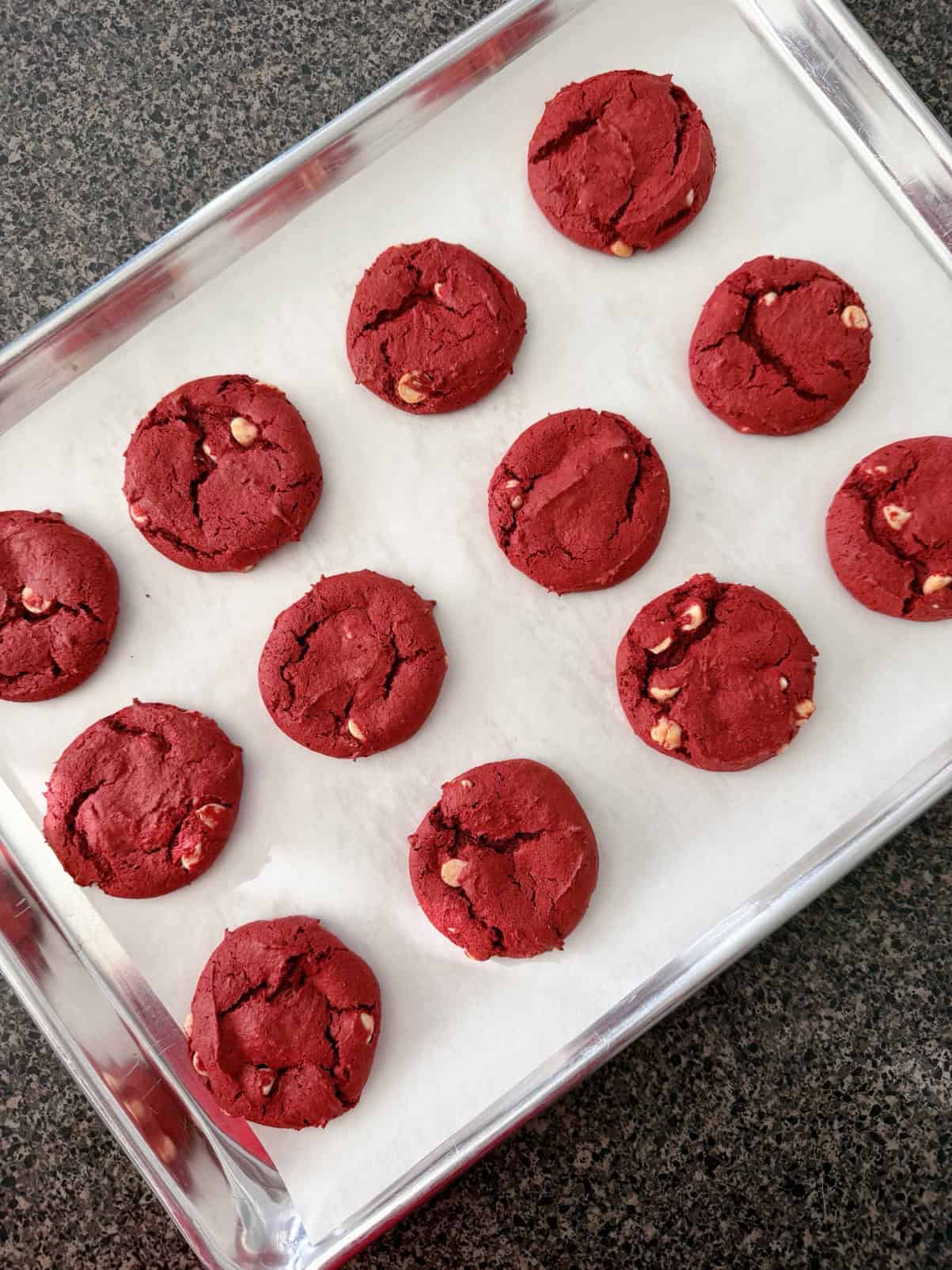 Red velvet cake mix cookies with white chocolate chips on a parchment paper-lined baking sheet.
