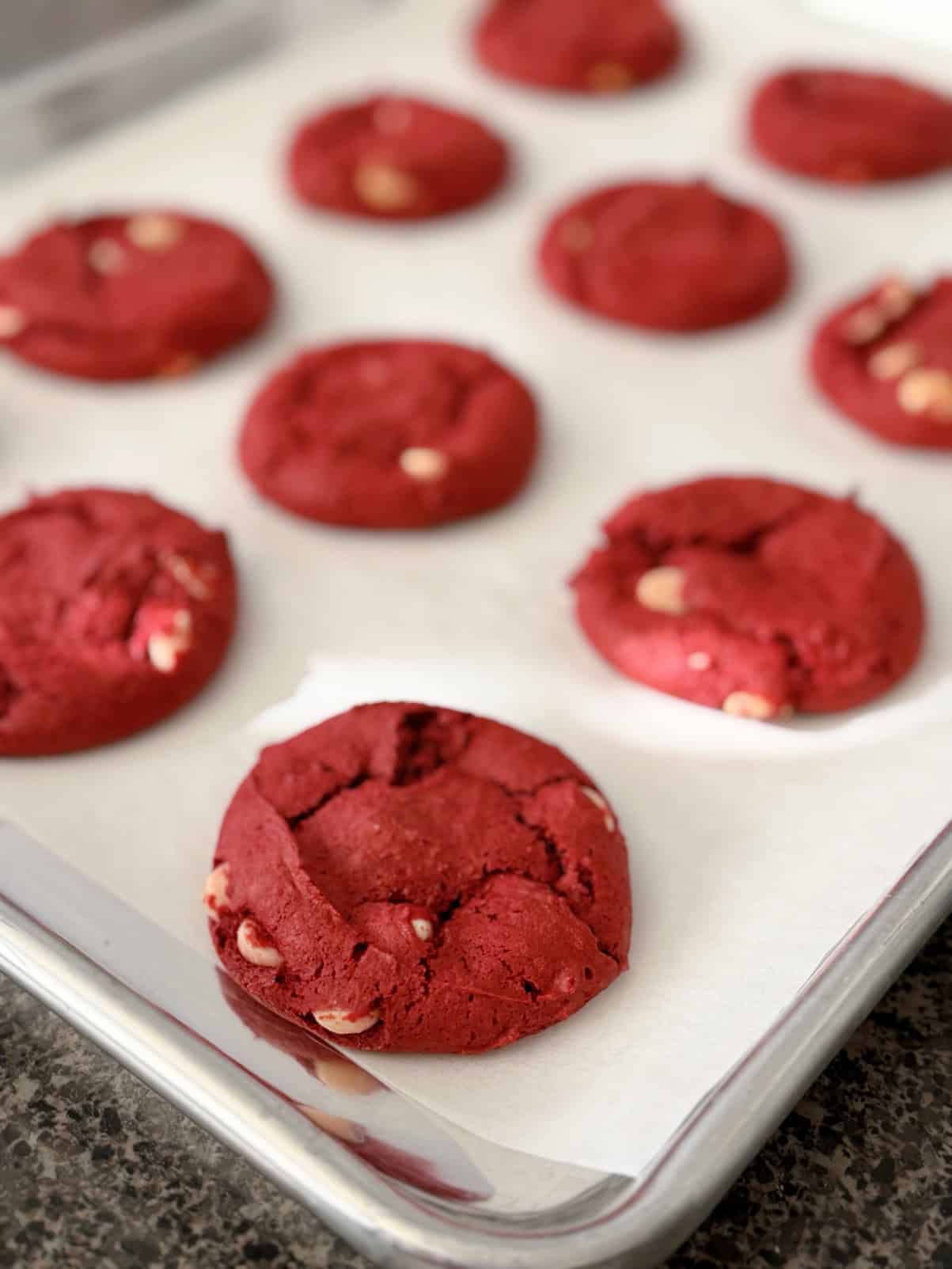 Red velvet cake mix cookies with white chocolate chips on a parchment paper-lined baking sheet.