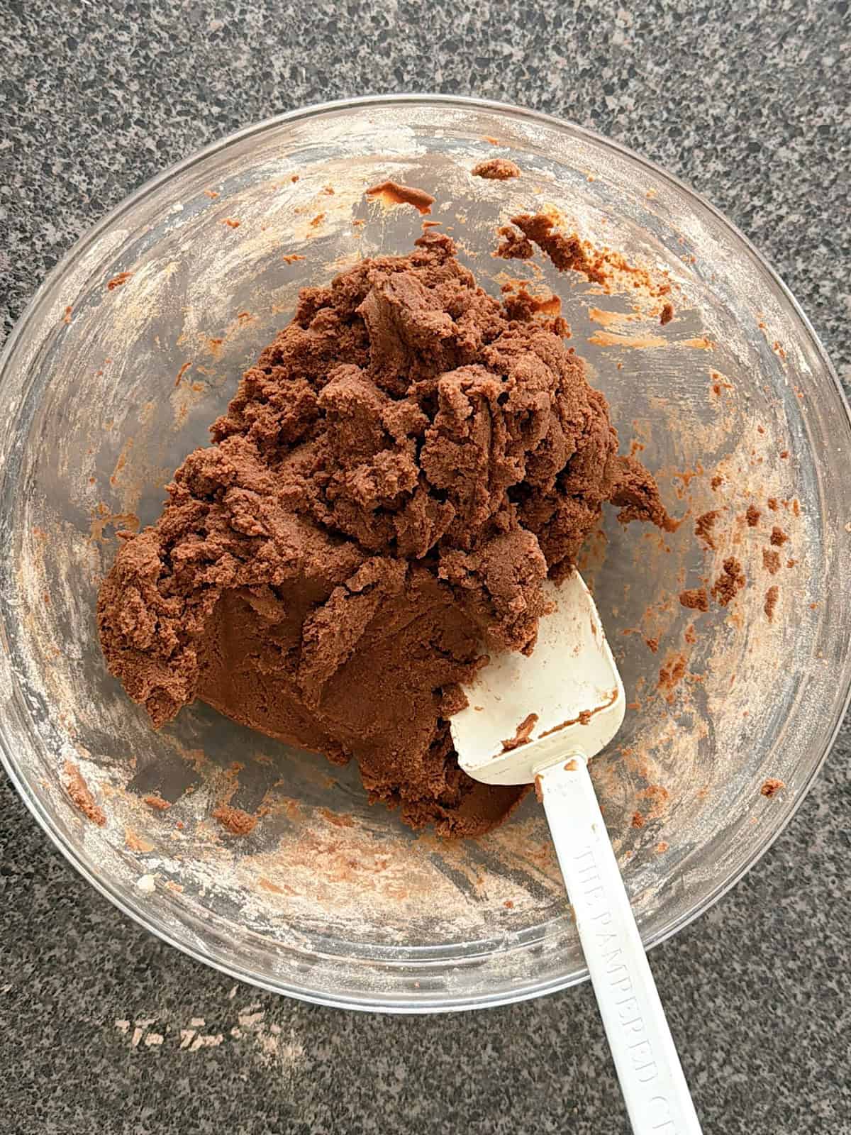 A bowl of chocolate cookie dough with a white spatula.