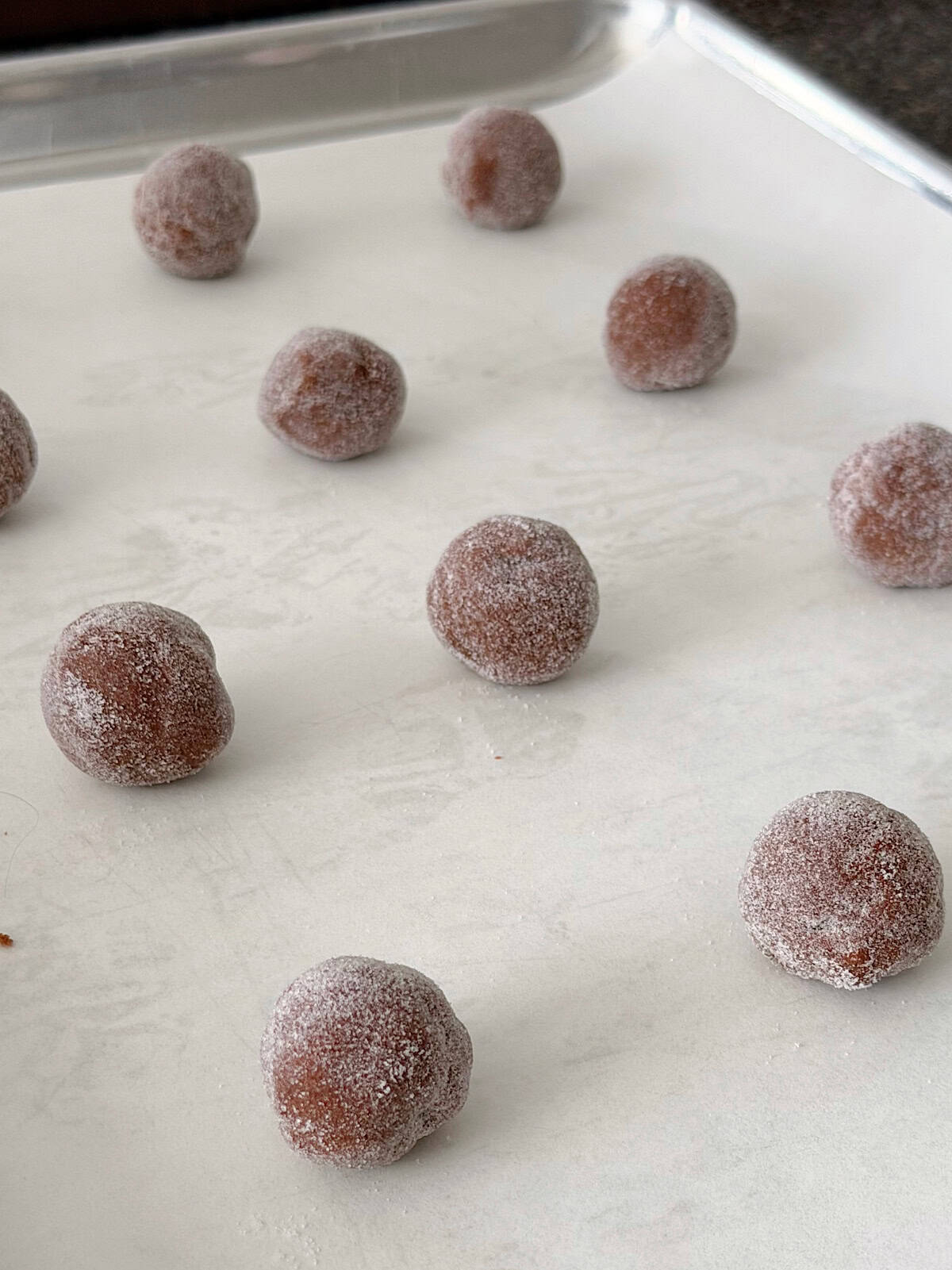 Chocolate cookie dough balls, coated in sugar, on parchment paper.
