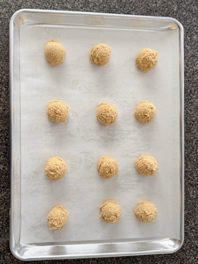 Eggnog cookie dough balls on a parchment paper-lined baking sheet.