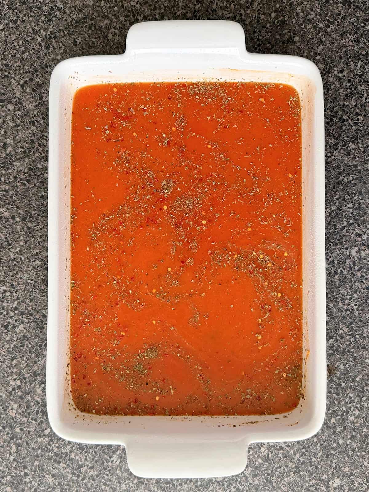 Spaghetti sauce and spices in a white baking dish.