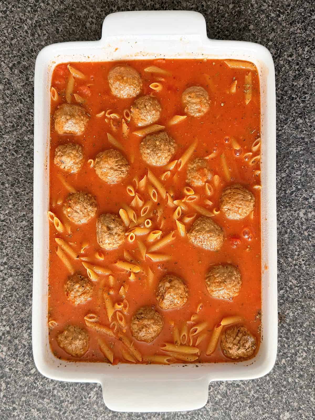Pasta, meatballs, and pasta sauce in a white baking dish.